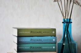 Poldark-kirjasarjan kirjoja pinossa hyllyllä sinisen maljakon vieressä.